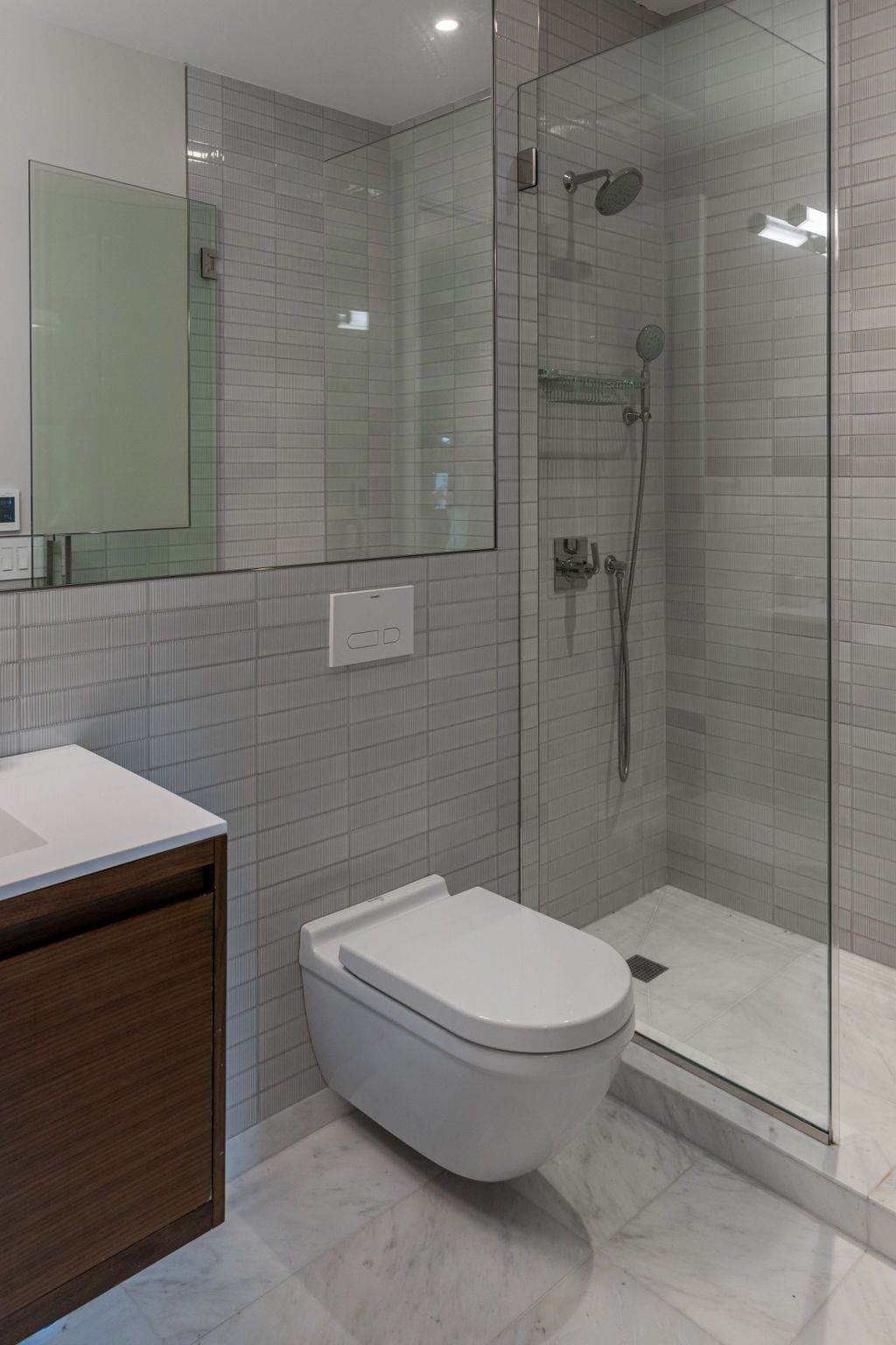 Modern bathroom with glass shower, toilet, and vanity. Gray tile walls and marble floor.