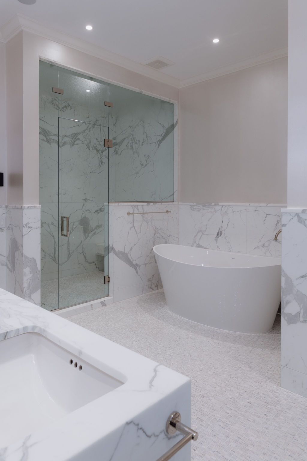 Spacious white bathroom with marble tile, a glass shower, and a freestanding oval bathtub.
