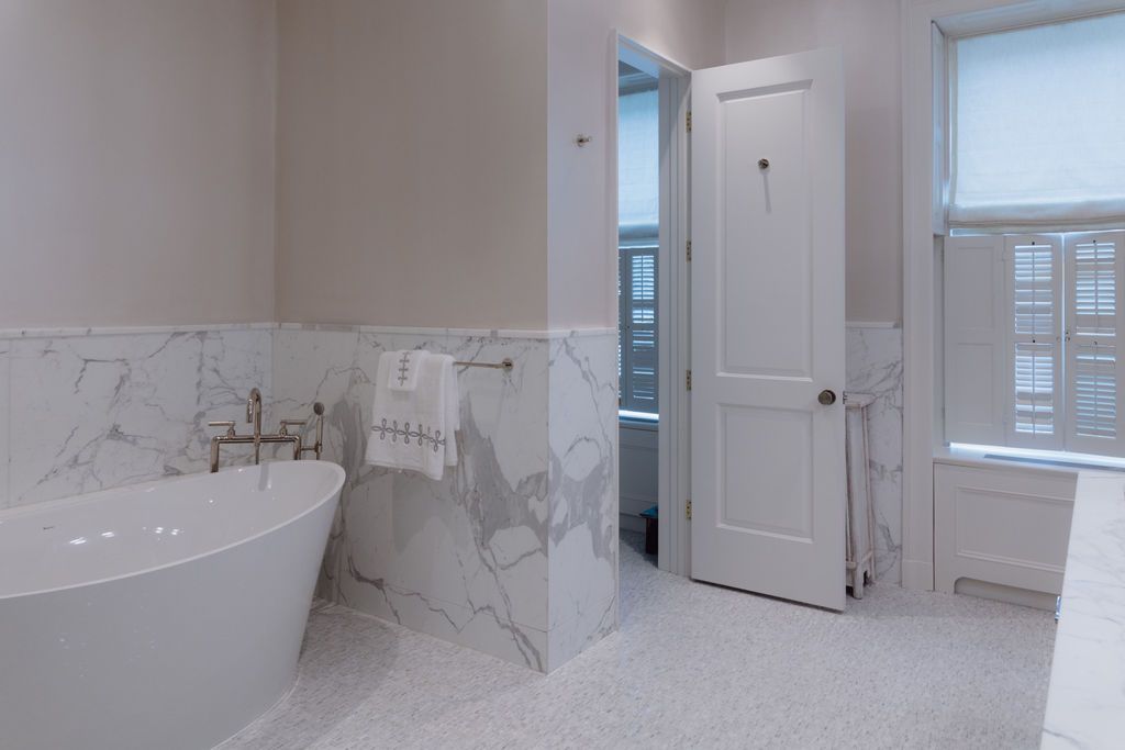 Modern bathroom with a white freestanding bathtub, marble tile, and a partially open door to a toilet.