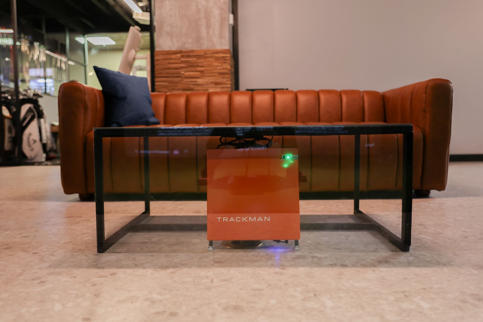 A brown leather couch with a black metal table, a brown box in front, and a blue pillow.