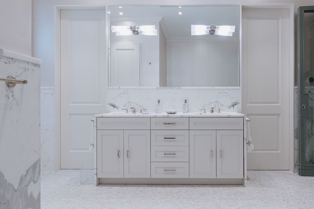 White bathroom with double sink vanity, large mirror, and two doors.