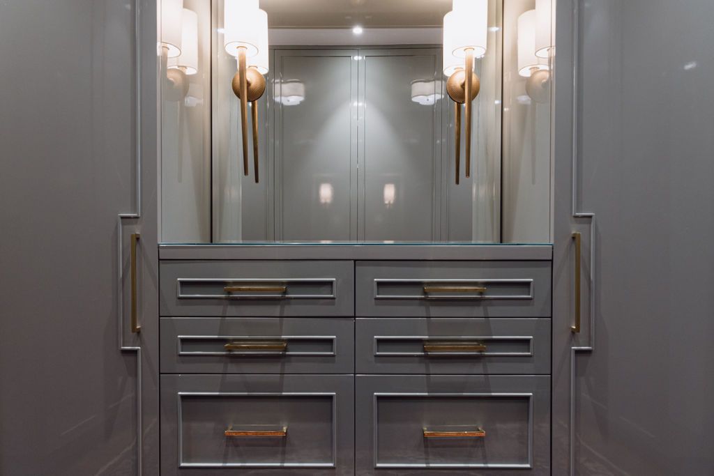 Gray built-in closet with drawers, a mirror, and gold sconces; neutral color palette.