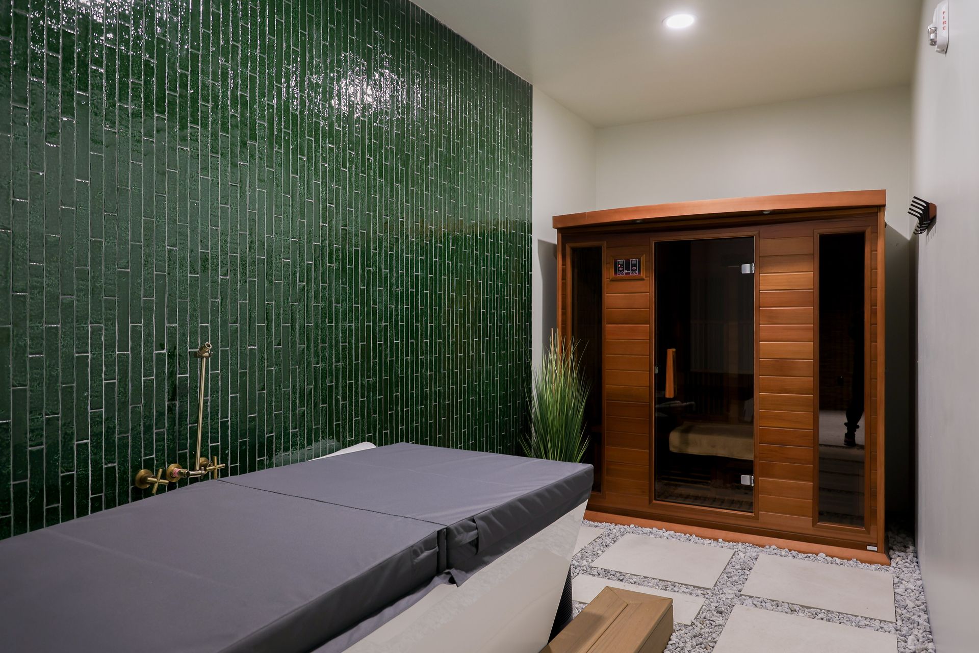A spa room with a massage table, sauna, and a green bamboo tile wall.