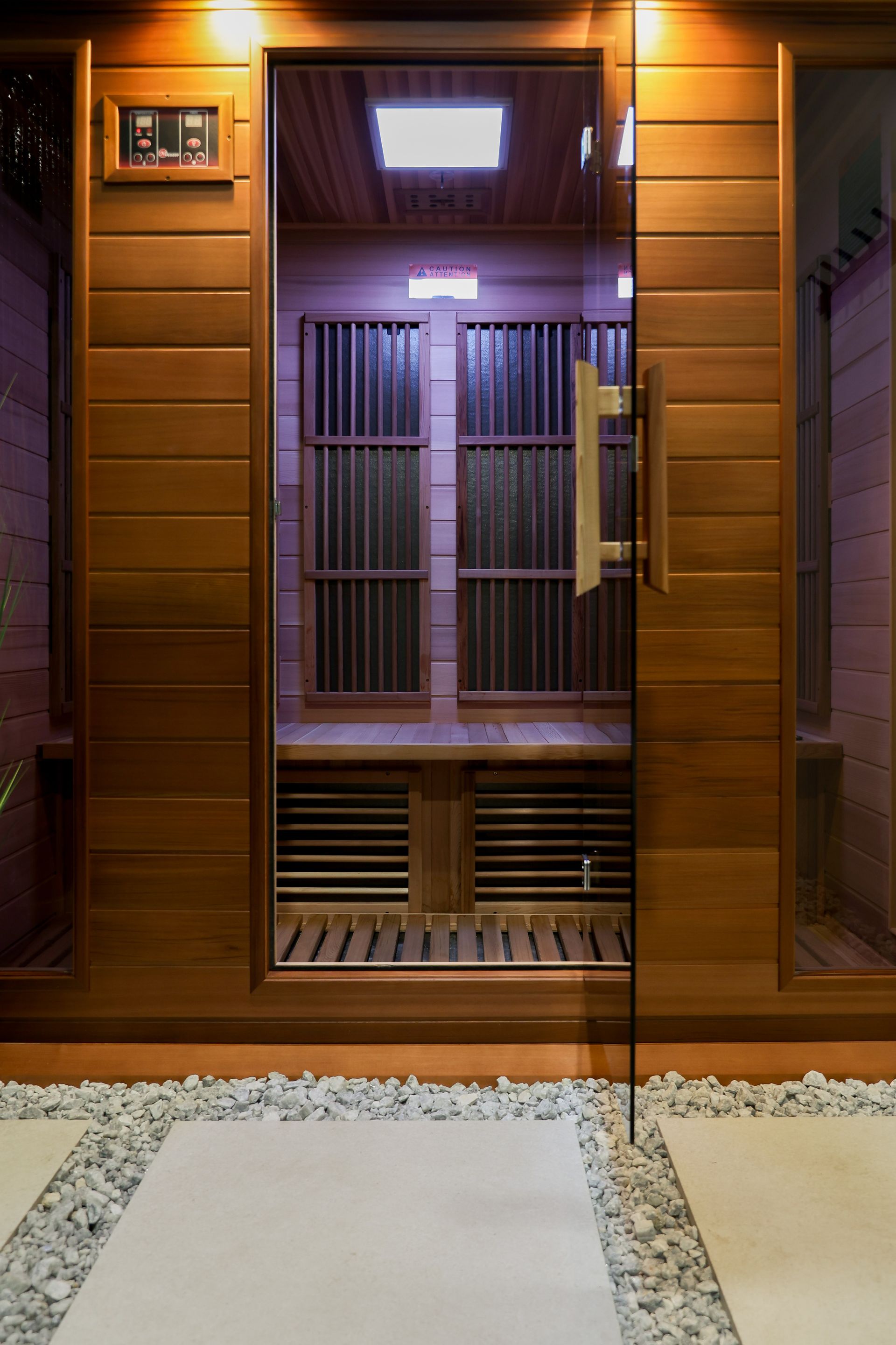 Wooden sauna with glass door, pebbles, and controls. Interior features wood benches and heating elements.