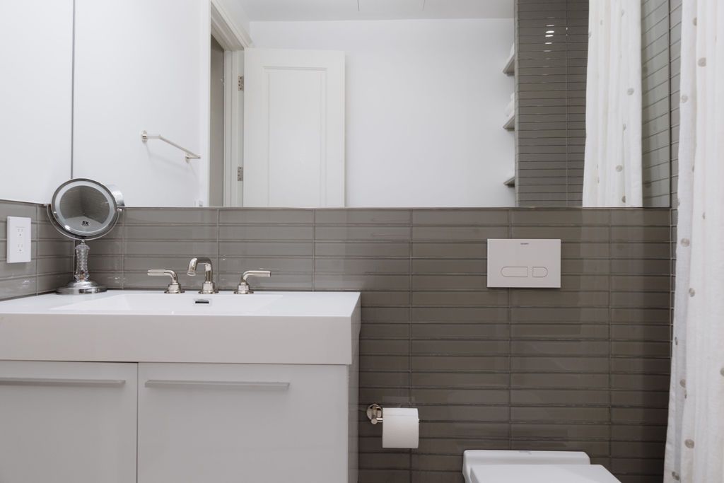 White bathroom with sink, mirror, toilet, and gray tiled wall.