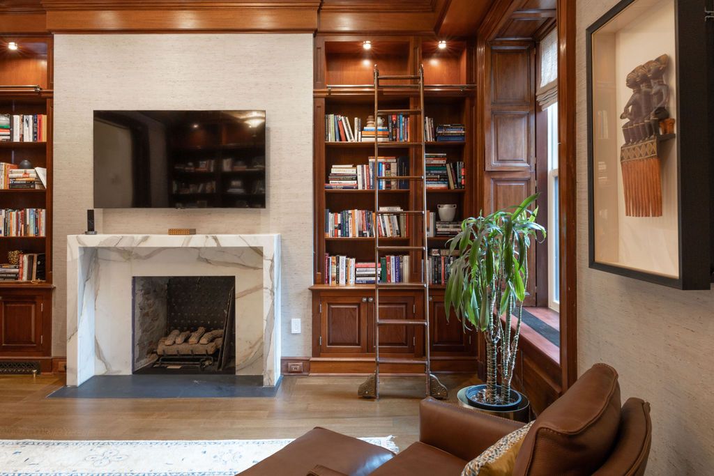 A library with a fireplace, built-in bookshelves, a rolling ladder, and a leather armchair.