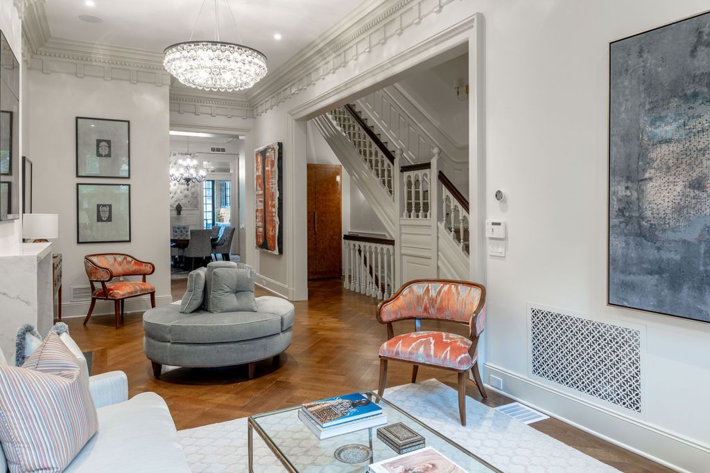 Elegant living room with hardwood floors, a round ottoman, and a staircase.