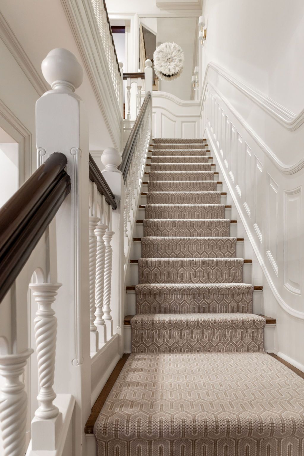 Staircase with carpeted steps, white banister, dark wood handrail, and white paneled walls.