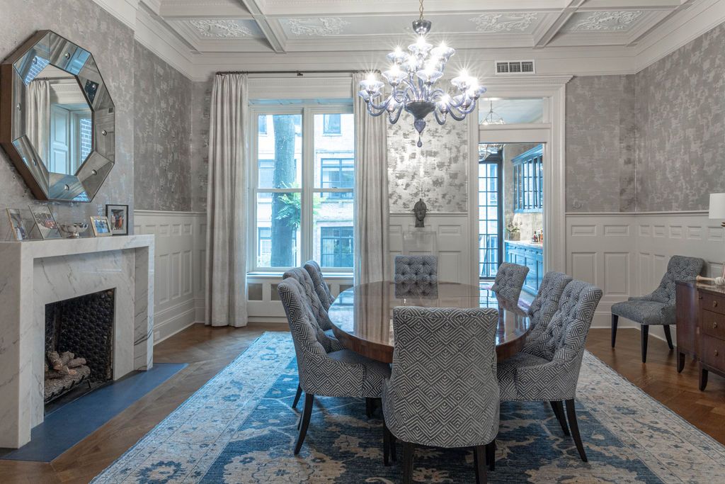 Elegant dining room with chandelier, oval table, patterned chairs, fireplace, and mirrored accents.
