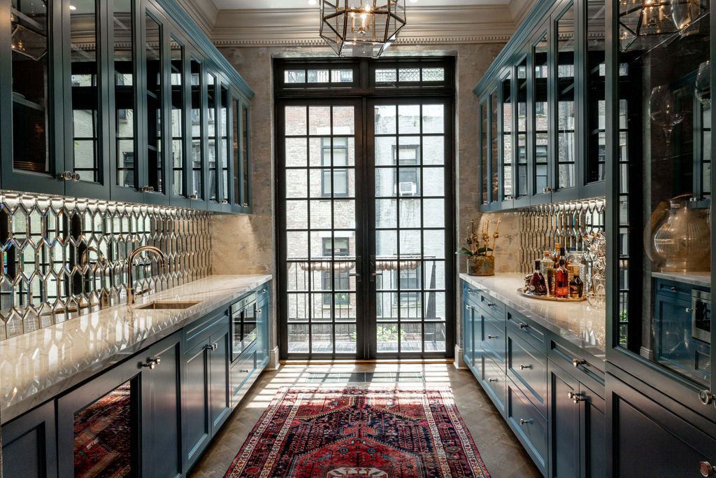 Blue-painted butler's pantry with cabinets, mirrored backsplash, rug, and French doors leading outside.