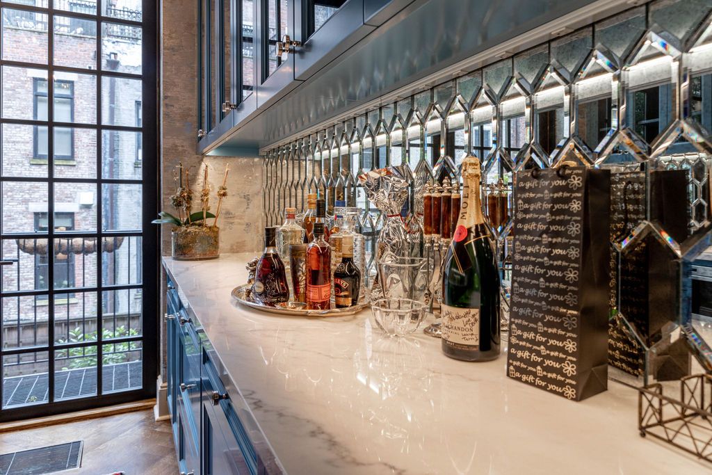 Bar with bottles, glassware, and decorative mirror tiles. Marble countertop, large window, and blue cabinets.