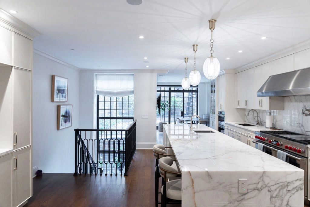 Luxurious white kitchen with marble island, staircase, and pendant lights.