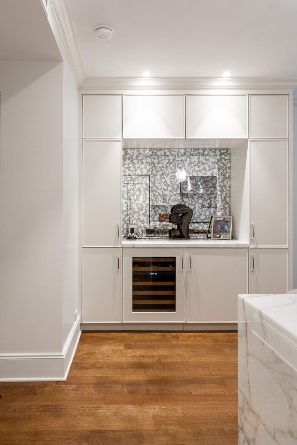 White cabinet bar area with a wine fridge, reflective backsplash, and wood floors.