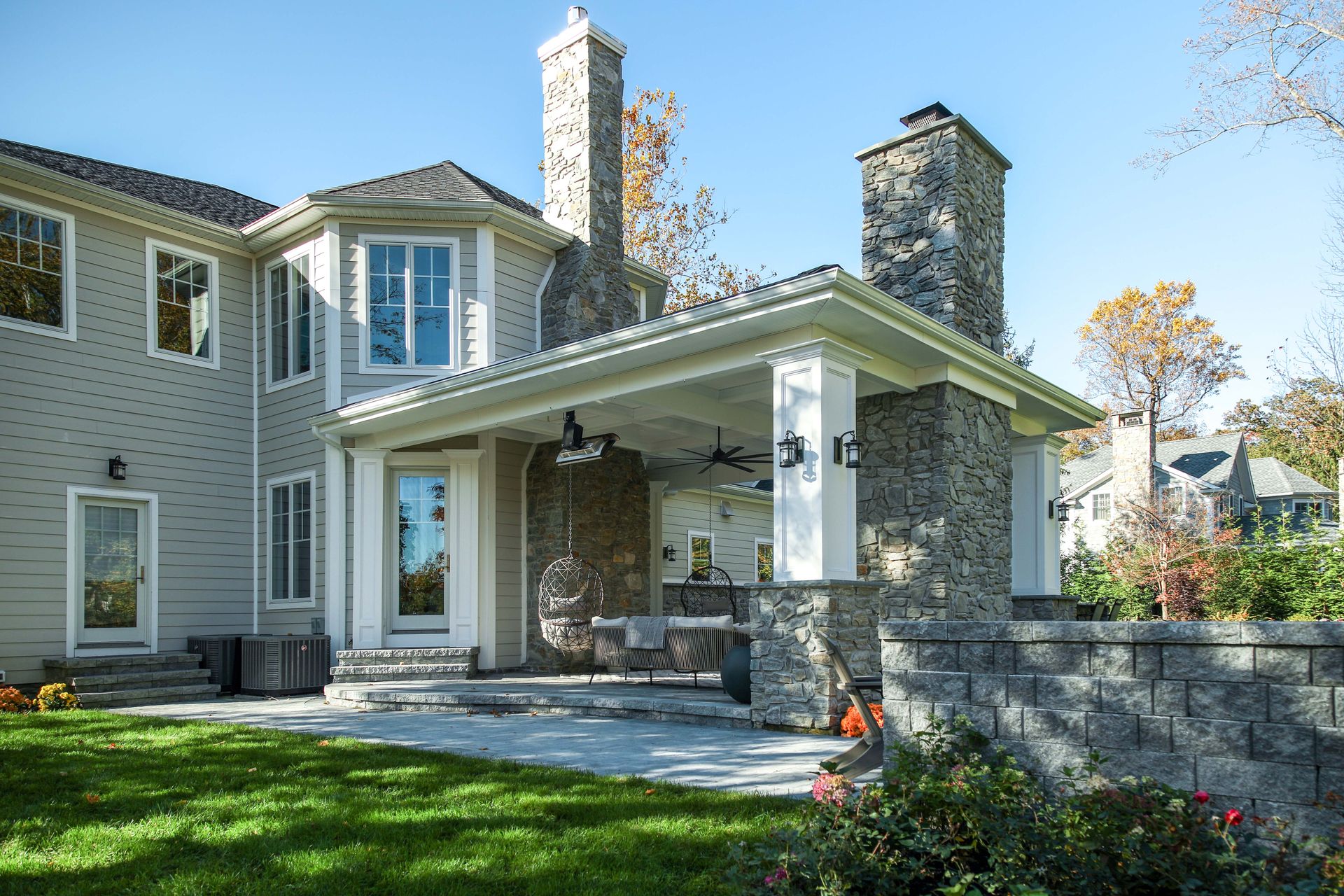 Exterior view of a house with a stone patio, roofed area, and chimneys on a sunny day.
