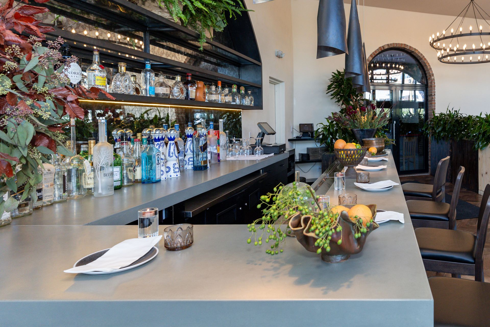 Bar interior with liquor bottles, a long counter, stools, and hanging lights.