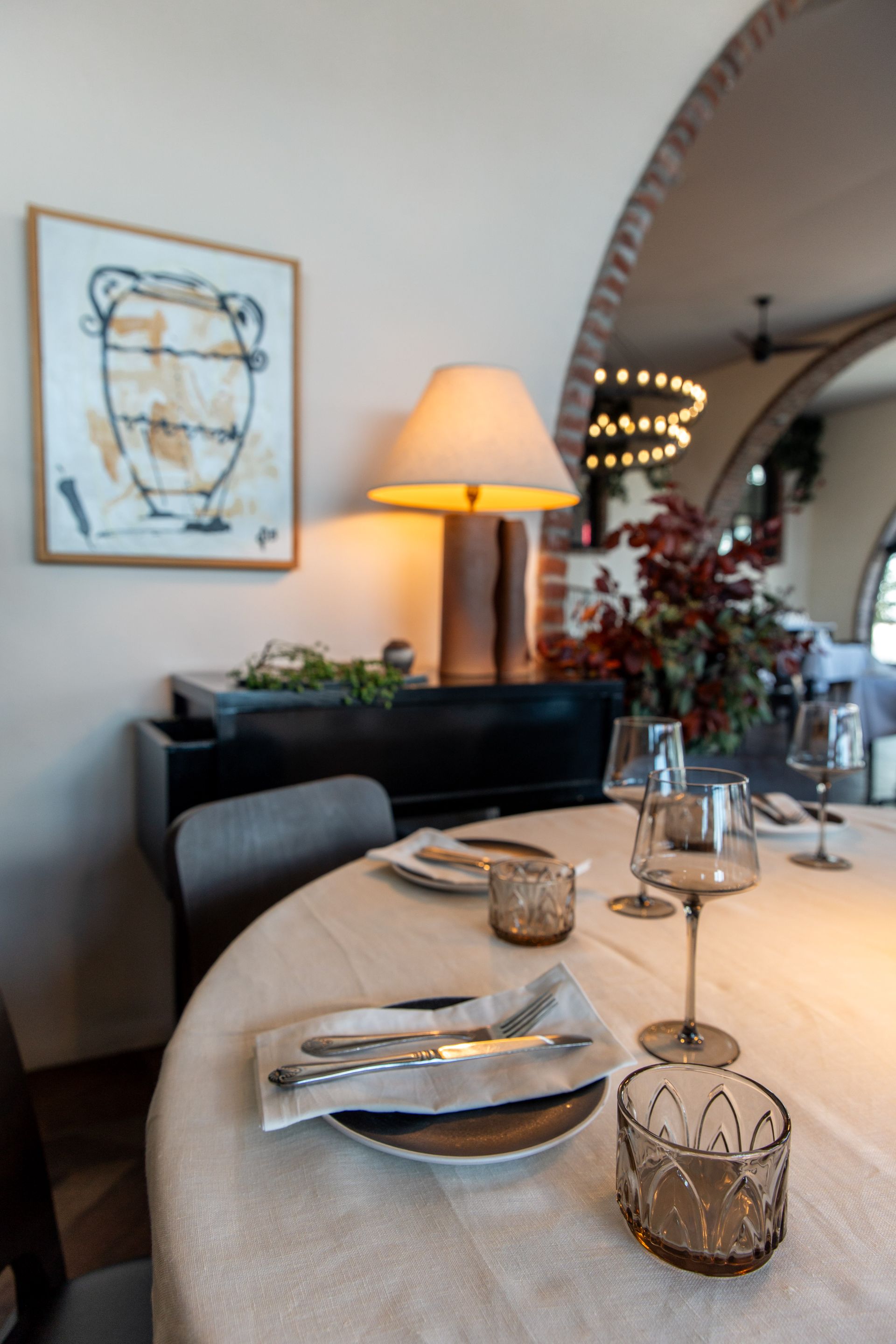 Elegant restaurant table setting with lamp, artwork, and arched doorway in background.