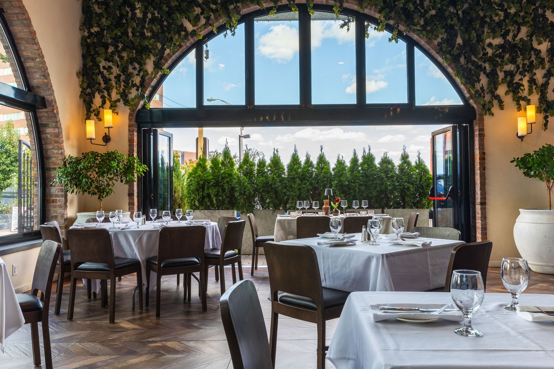 Interior of a restaurant with tables set for dining, arched doorway open to outdoor greenery.