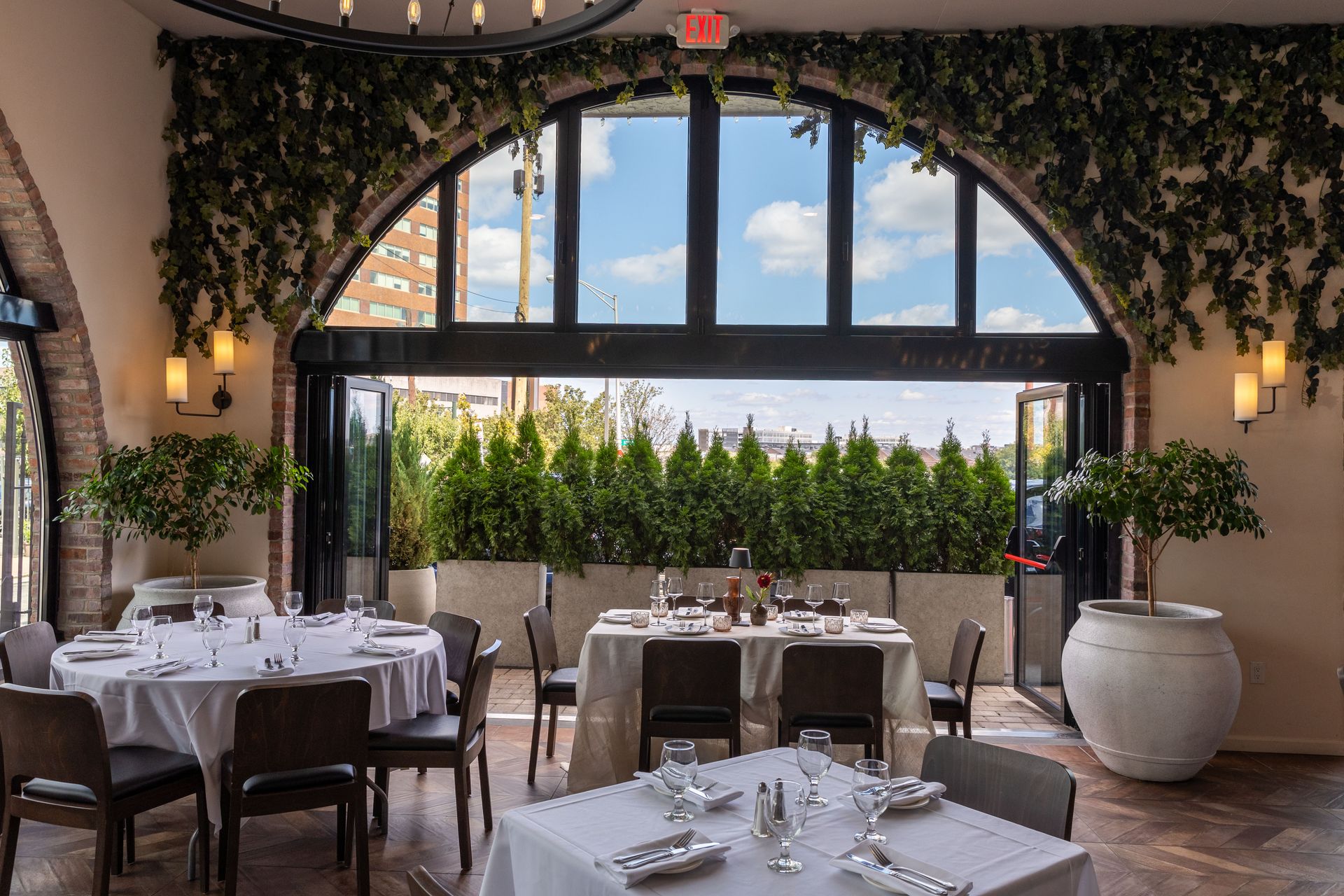 Restaurant dining room with arched doorway, white tablecloths, and a view of greenery outside.