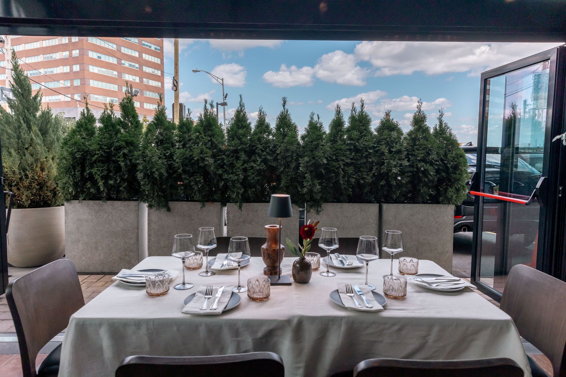 A restaurant table set for a meal, with a city view and green shrubs in the background.