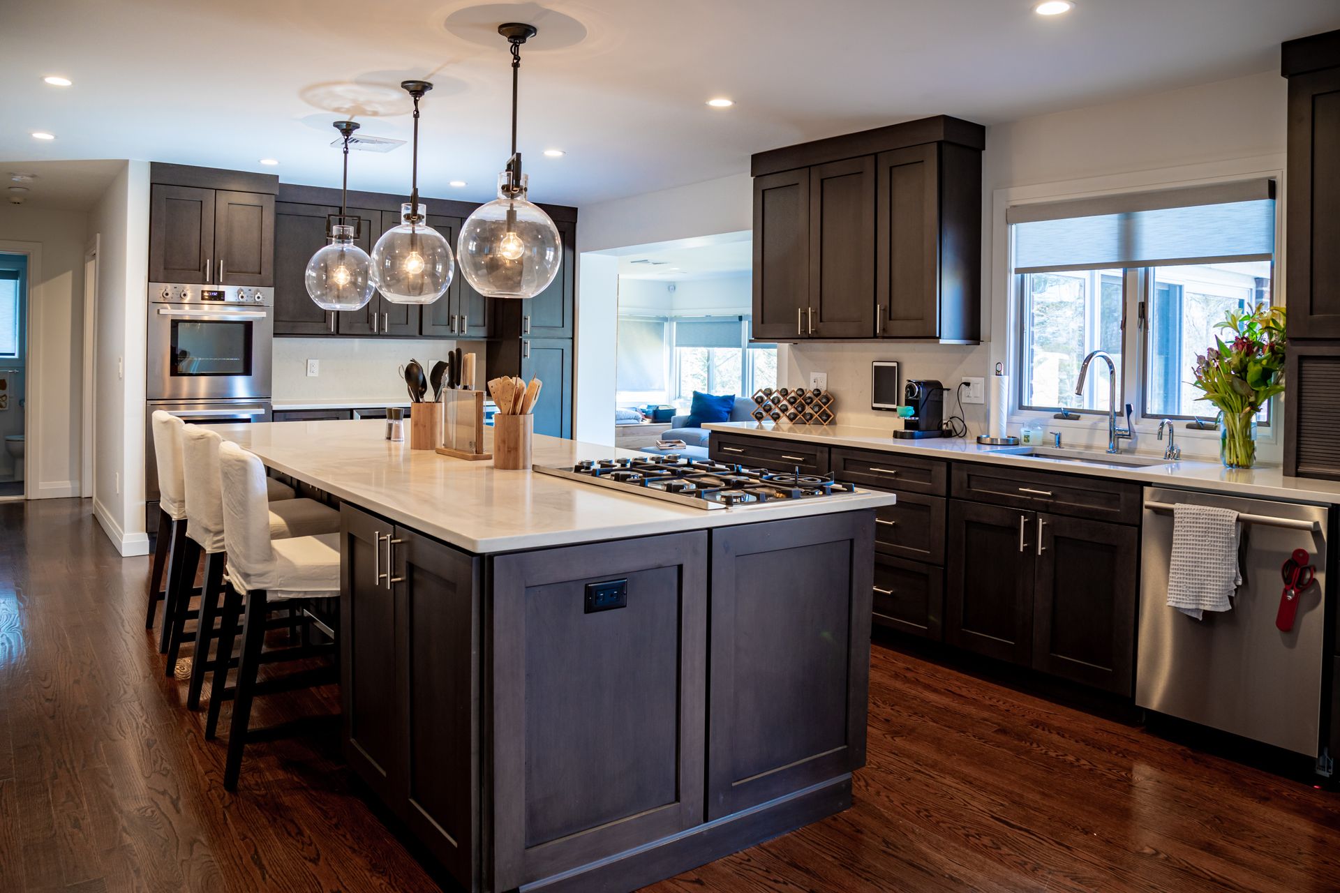 Kitchen with dark brown cabinets, white countertops, island with stovetop, and pendant lights.