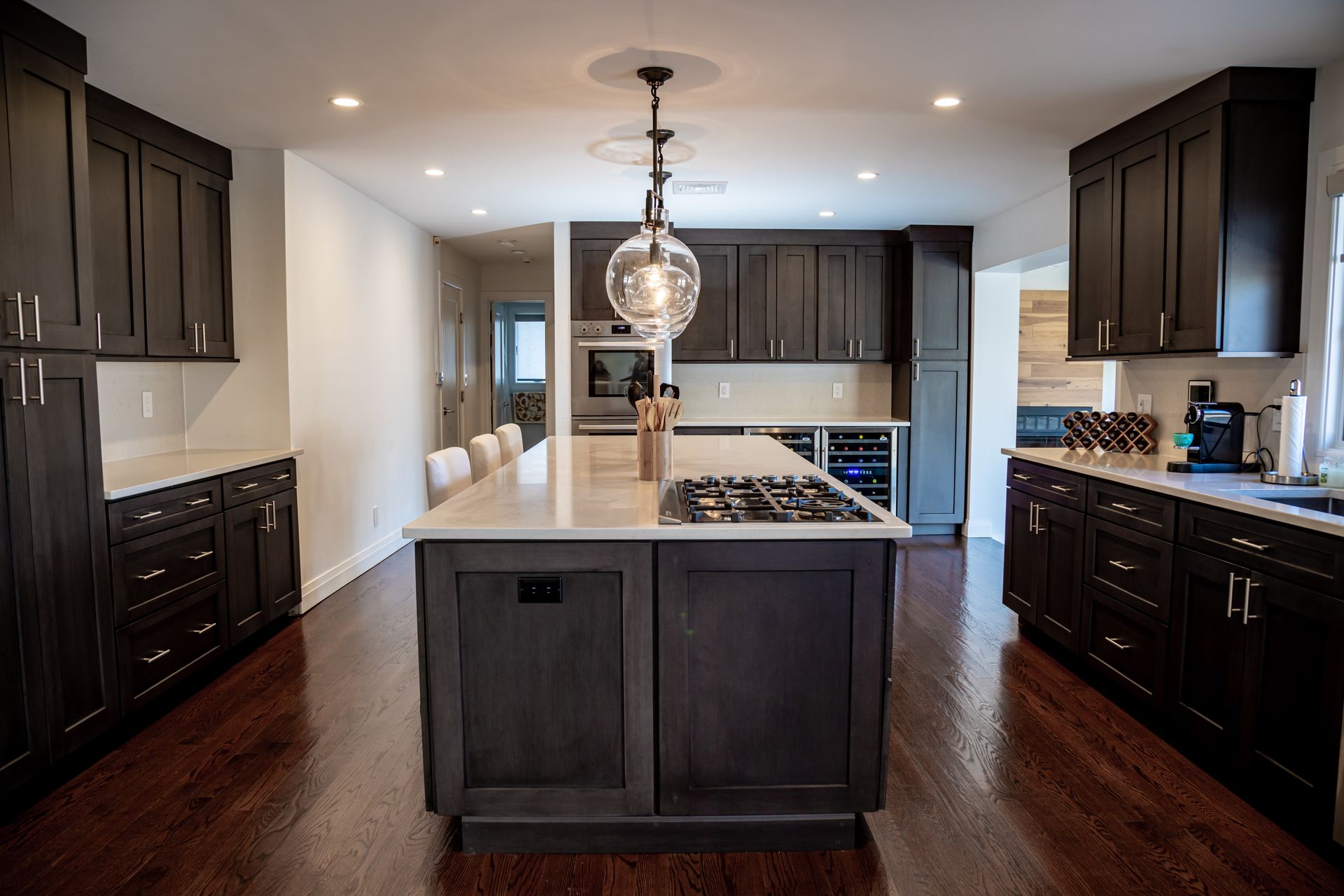 Dark-toned kitchen with island and overhead light, cabinets, and hardwood floors.