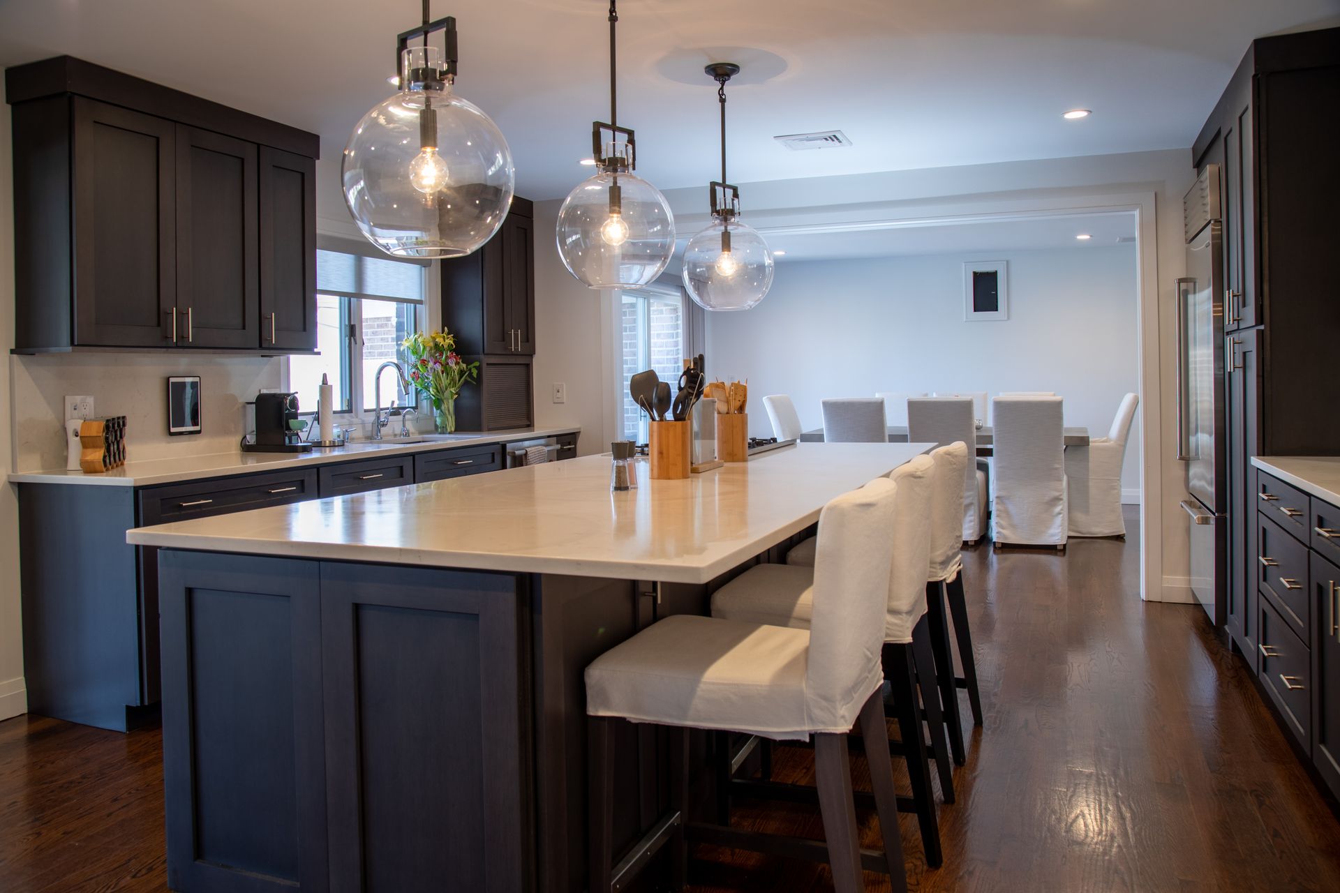 Kitchen with dark cabinets, white countertop island, and pendant lights. A dining room is visible beyond.