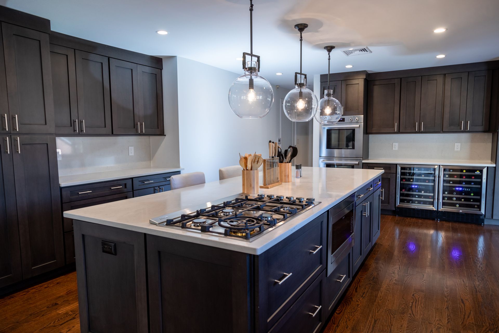 Modern kitchen with dark cabinetry, white countertops, and a central island with a stovetop.