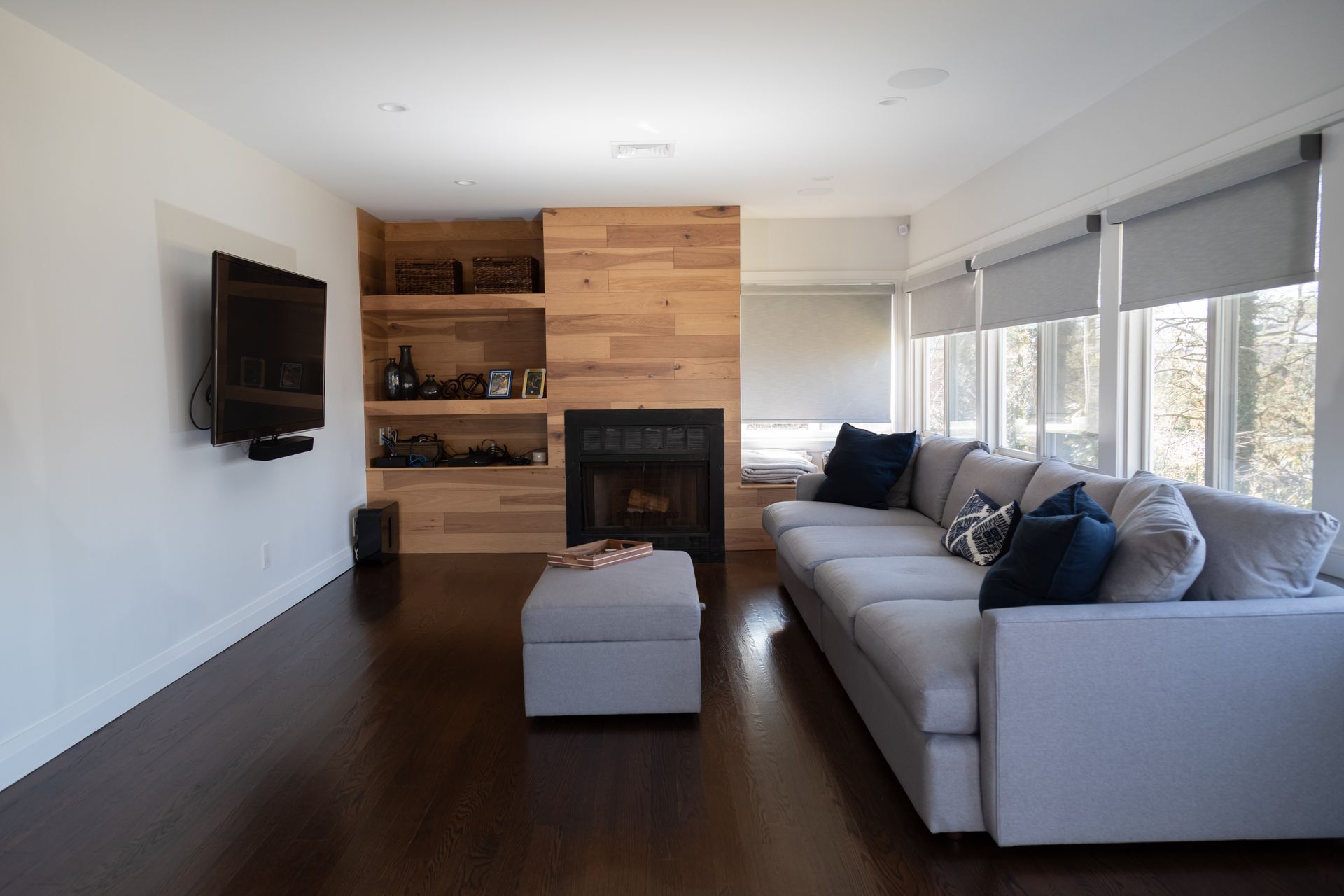 Living room with wood panel fireplace, built-in shelves, large gray sectional sofa, TV, and dark wood floors.