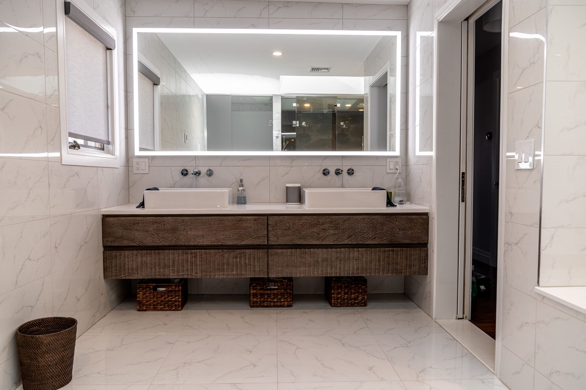 Modern bathroom with a double sink vanity, large mirror with lights, and marble tile.