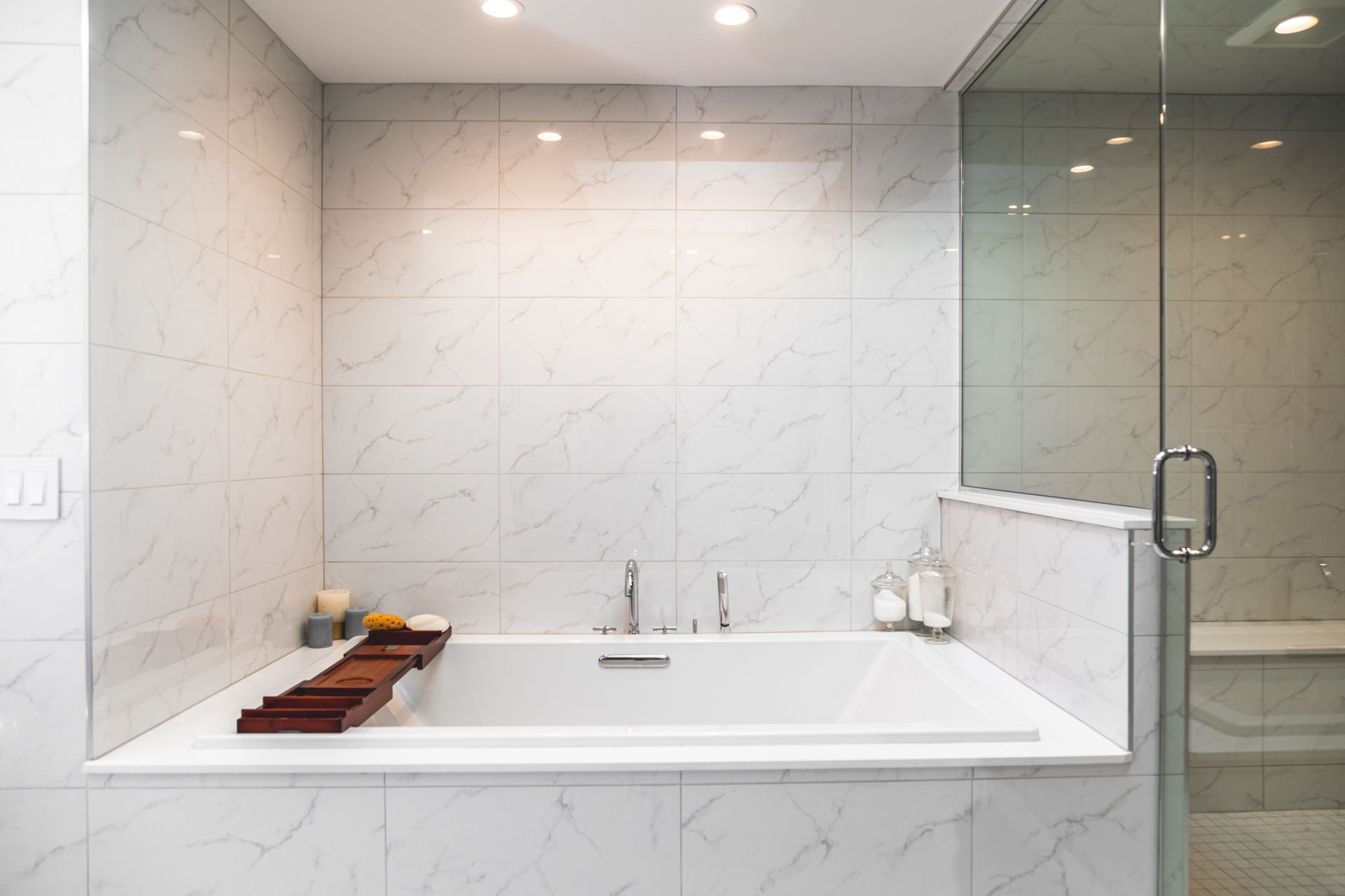 Modern bathroom with white marble tile, bathtub, and glass shower door.