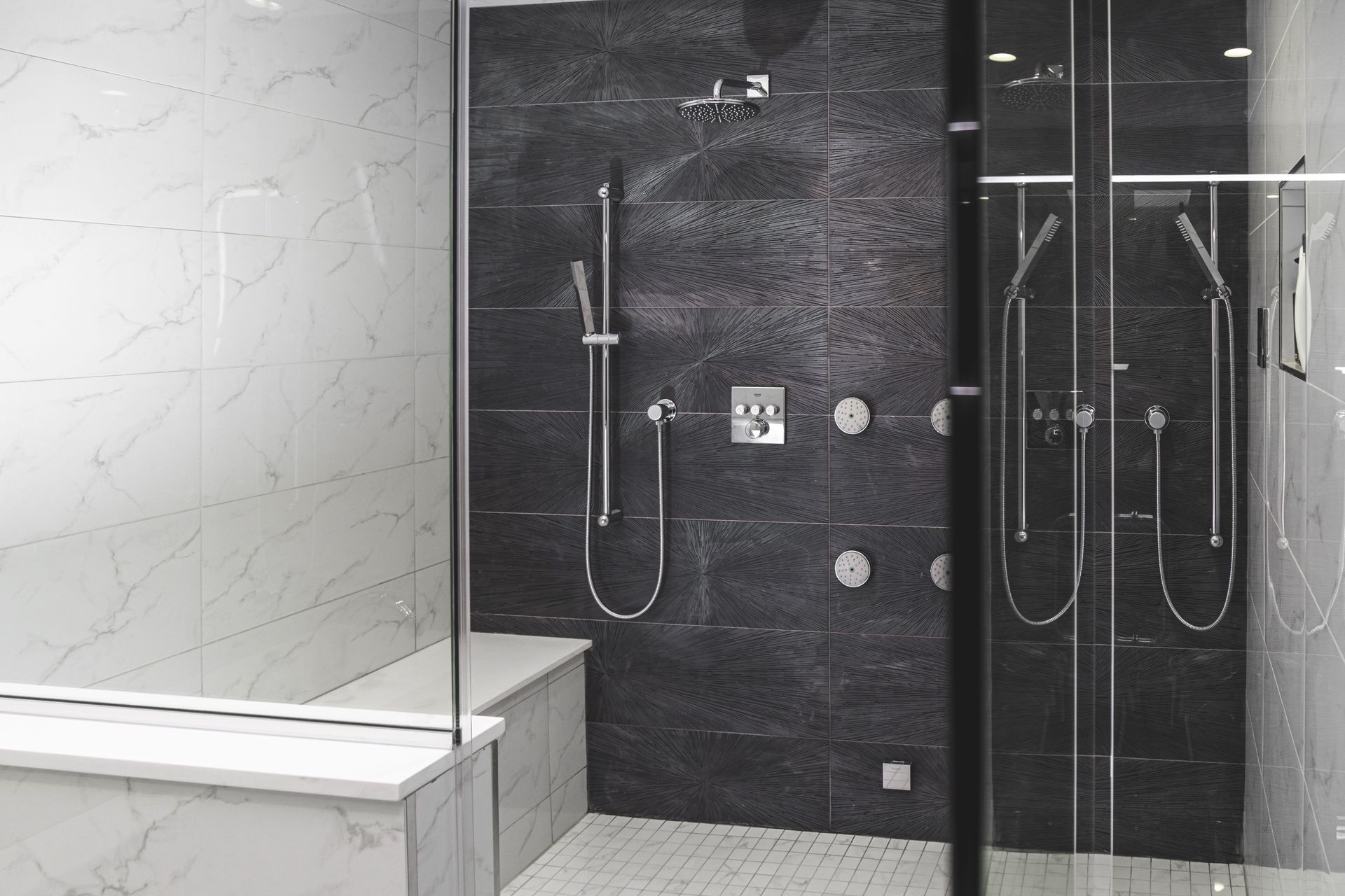 Modern shower with black tiled wall, glass doors, and white bench.