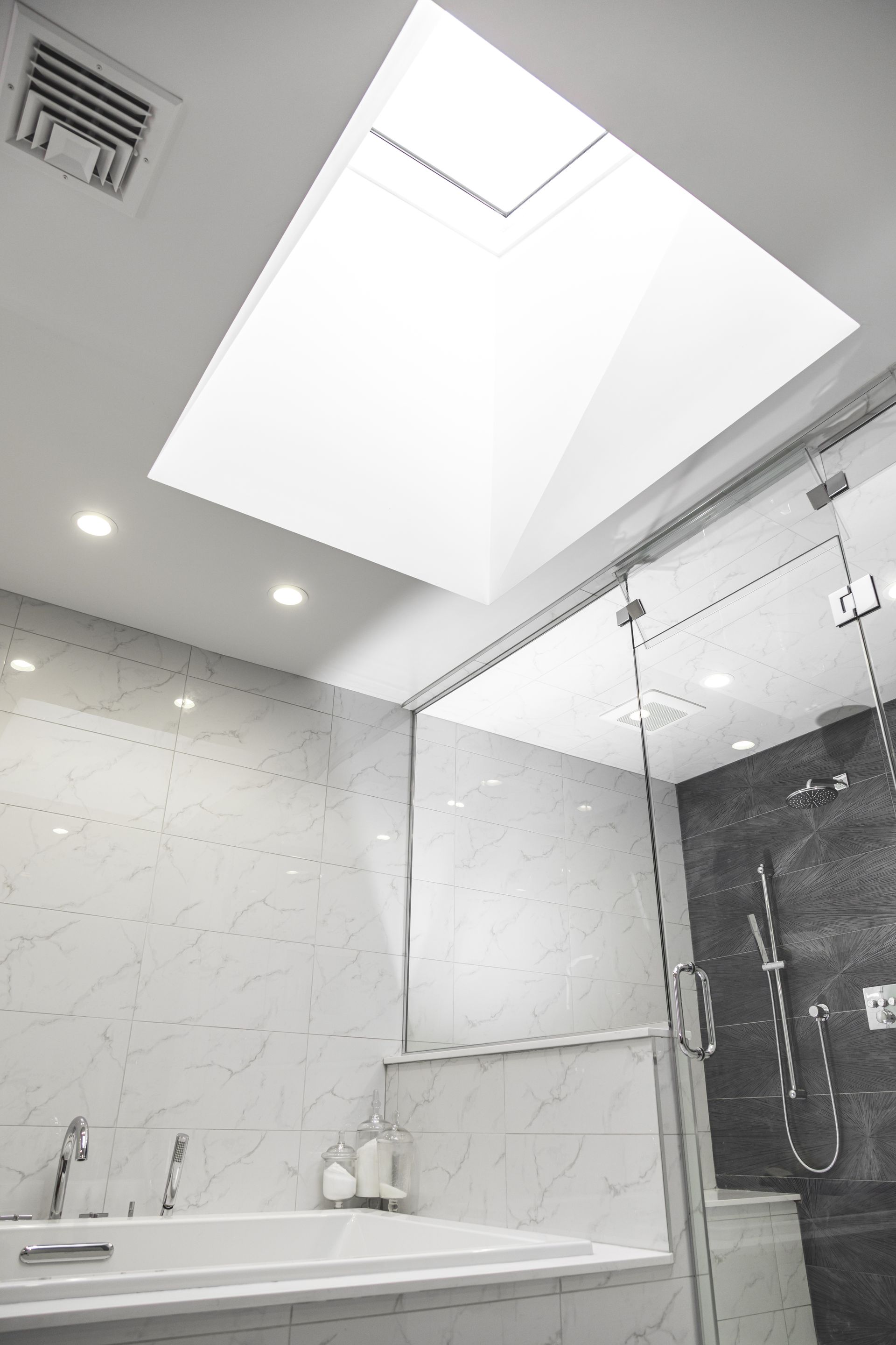 Bathroom with skylight, white and gray marble walls, glass shower, and soaking tub.