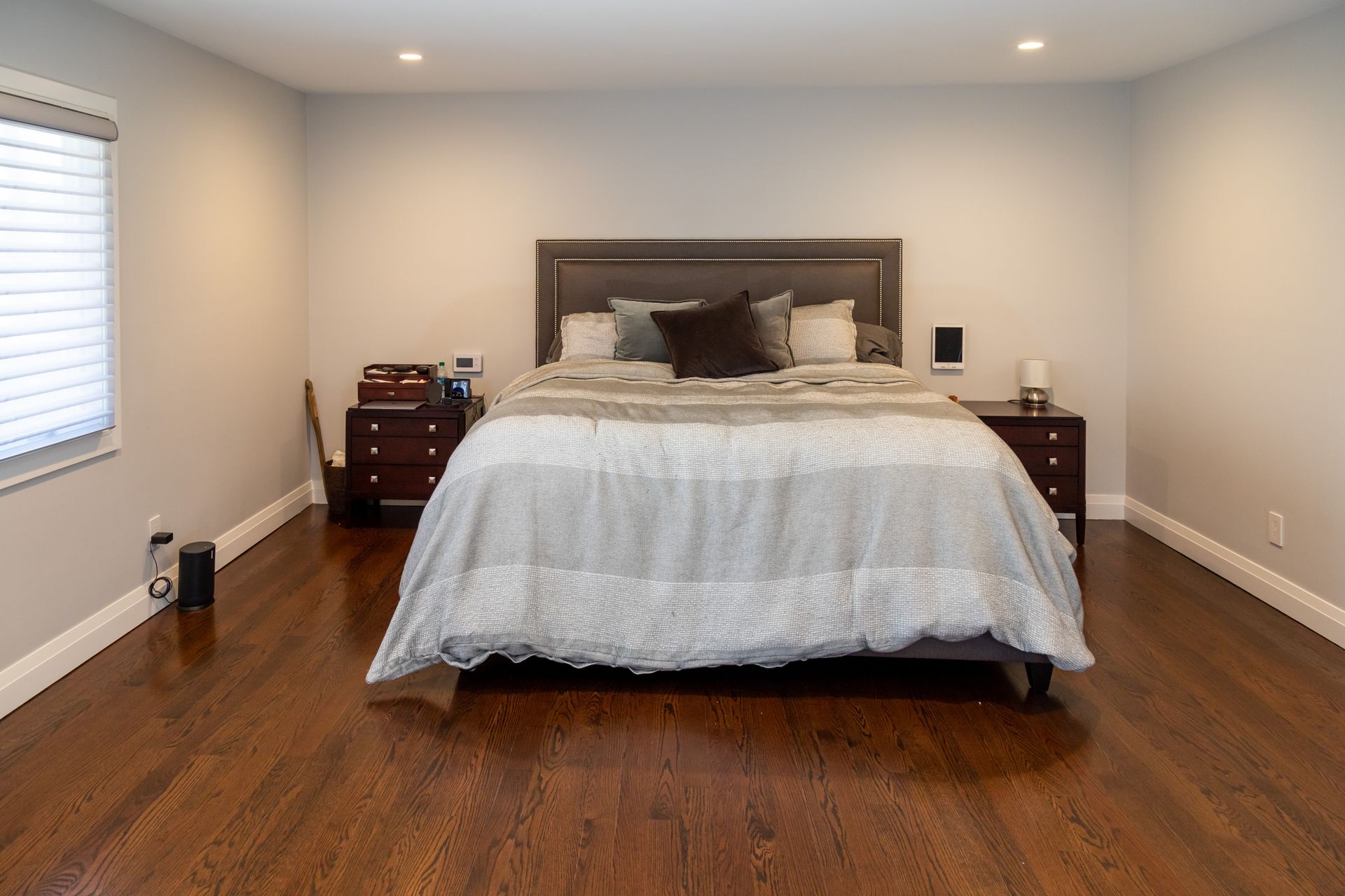 Bedroom with bed centered, hardwood floors, nightstands, and window with blinds.