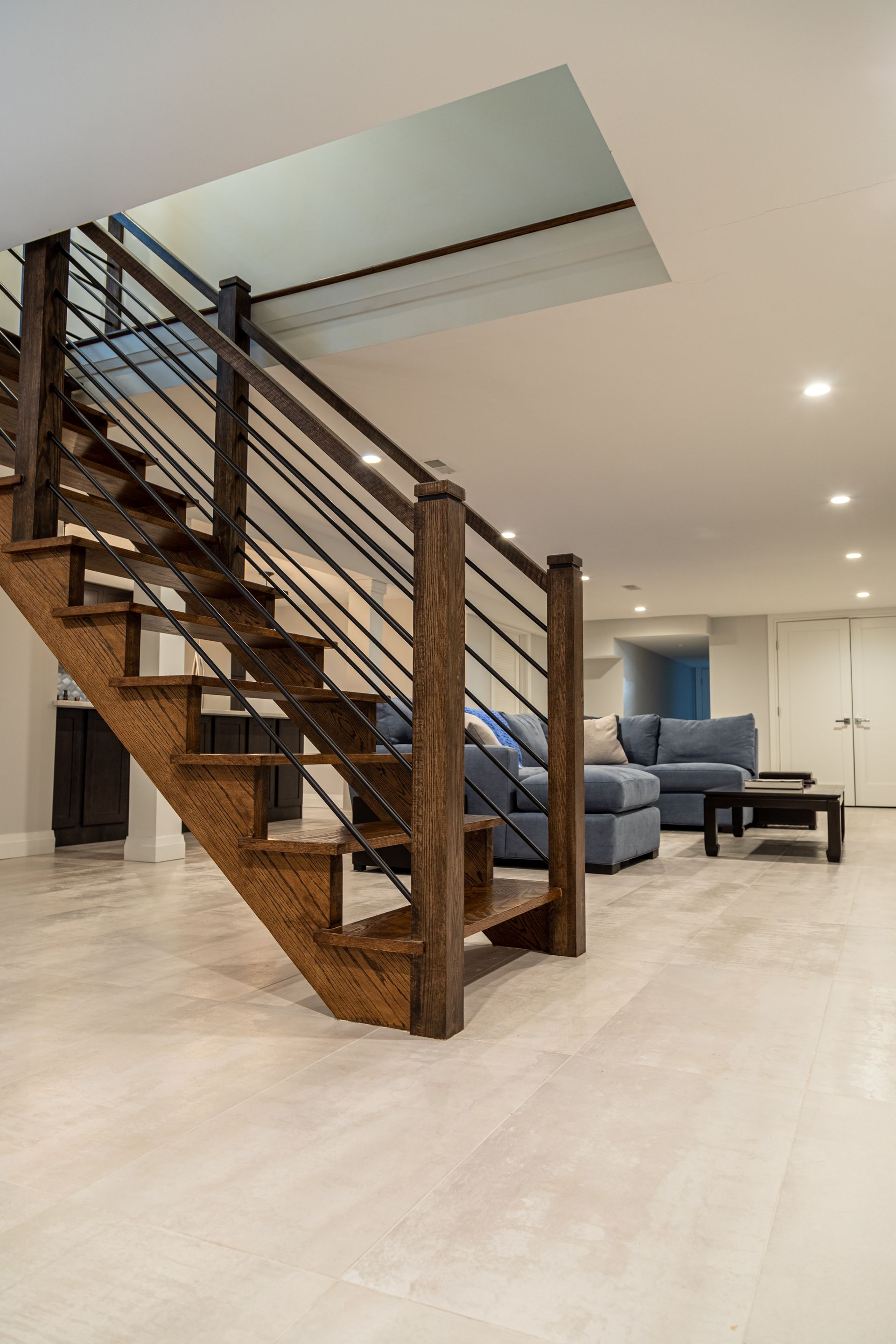 Wooden staircase with black railings leading to a light-filled living area with blue sofa and coffee table.