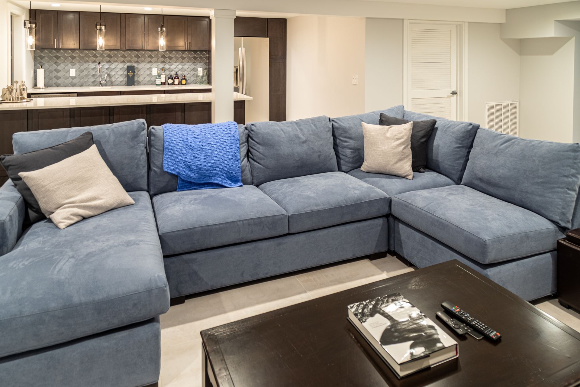 Blue sectional sofa in a modern living room with a coffee table and kitchen in the background.