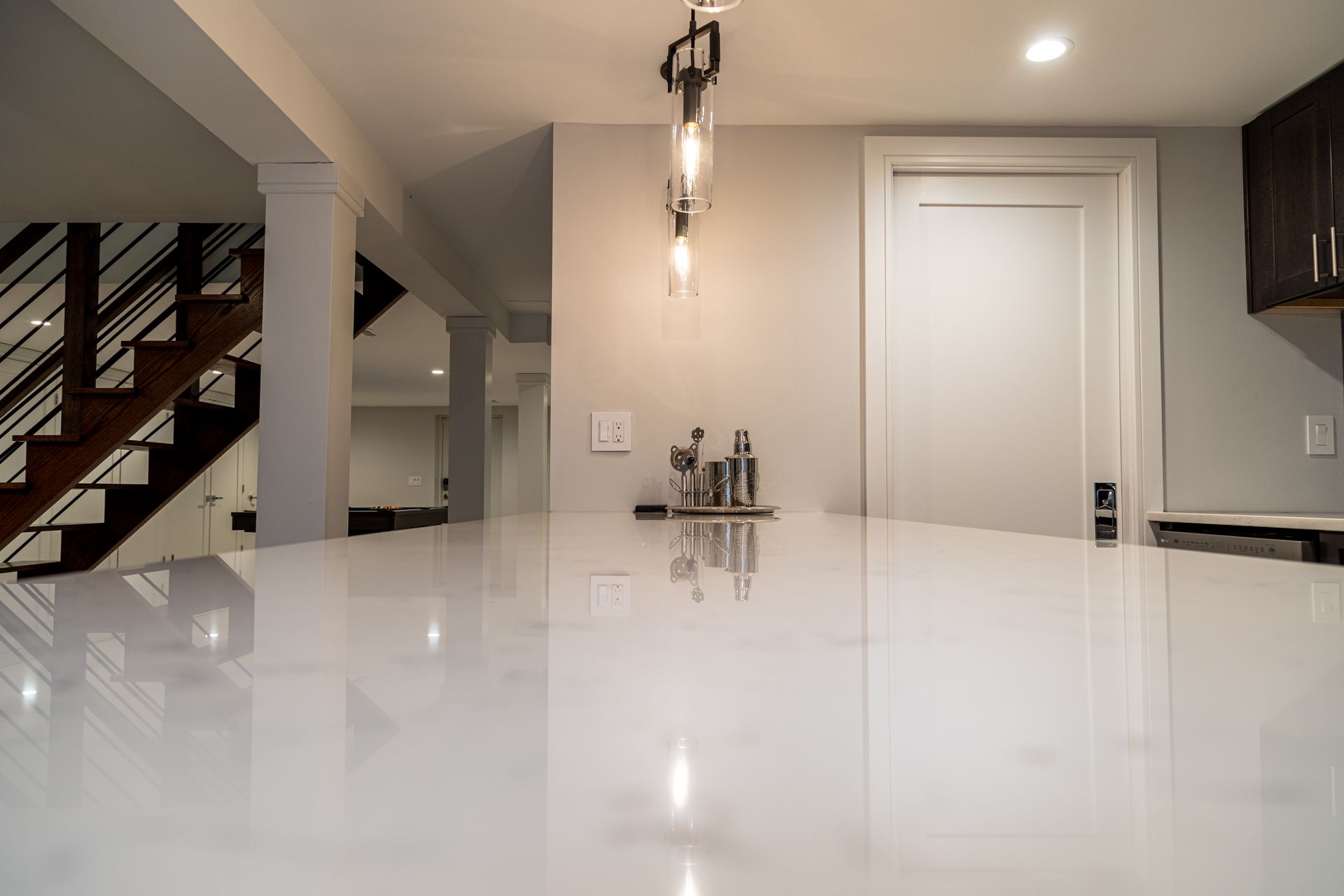 White countertop in a kitchen with a staircase, lights, and door in the background.
