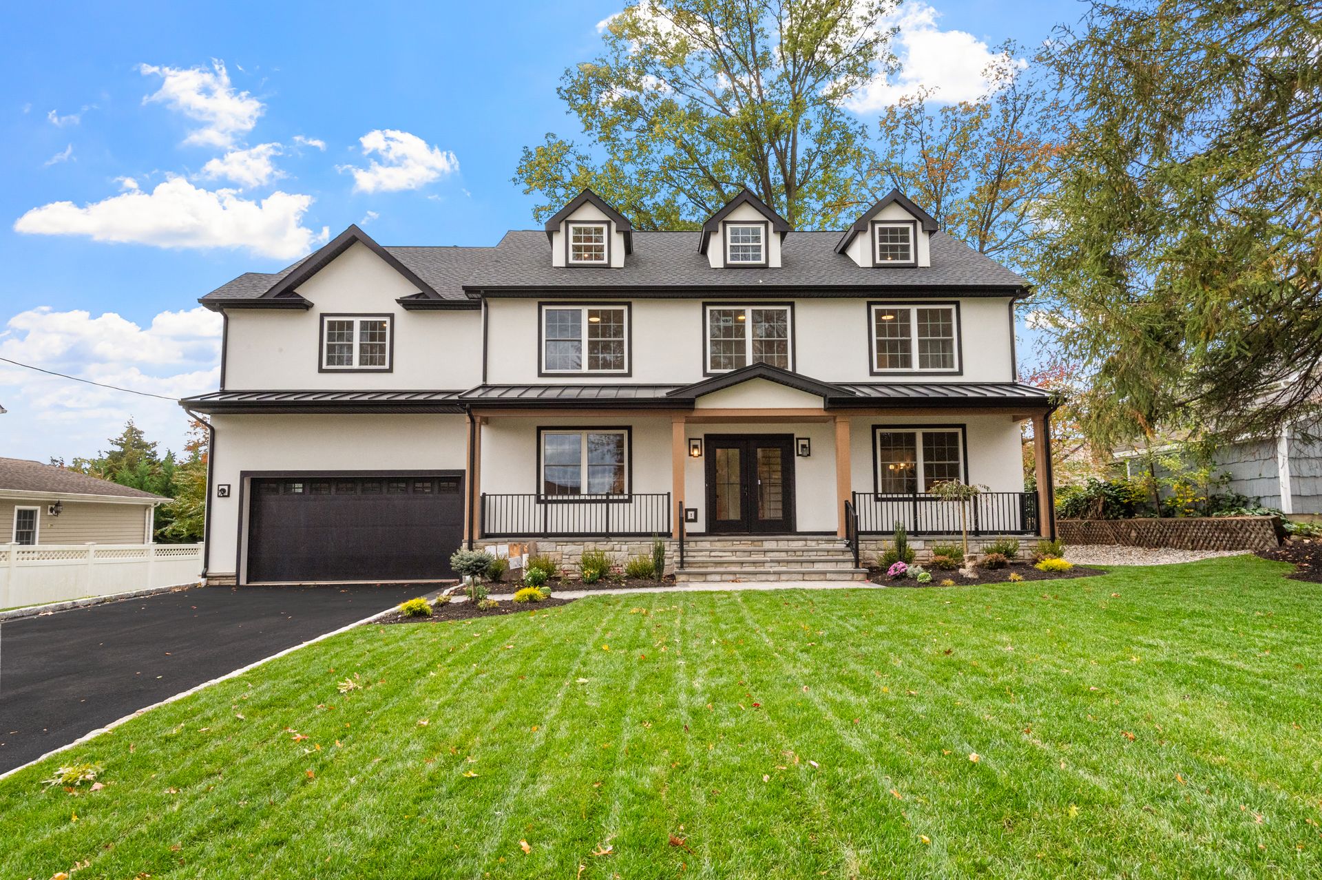 White house with black trim, a garage, and a green lawn under a blue sky.