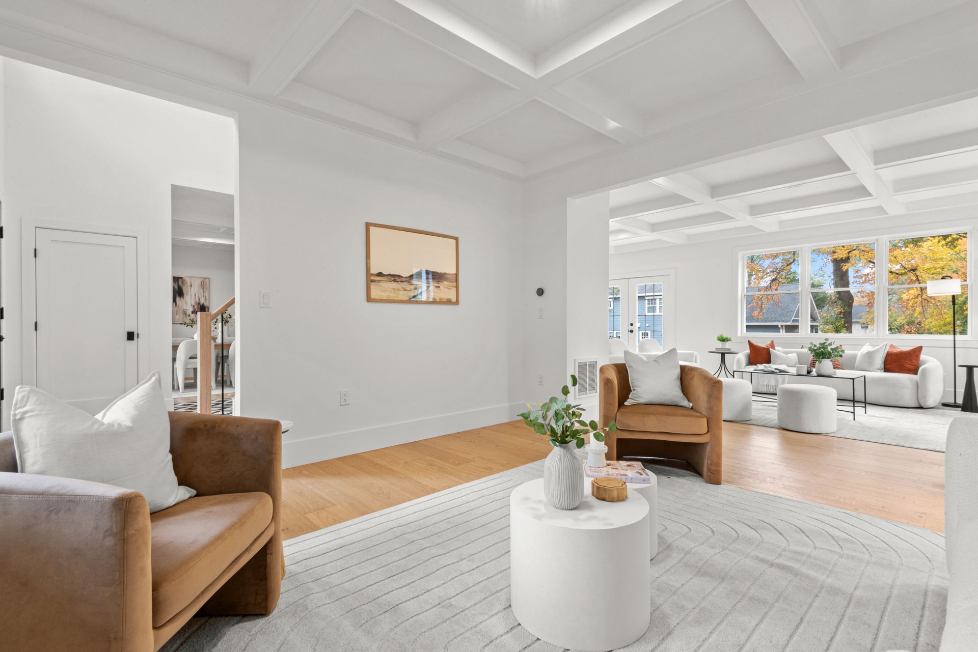 Living room with tan armchairs, white rug, and coffered ceiling.