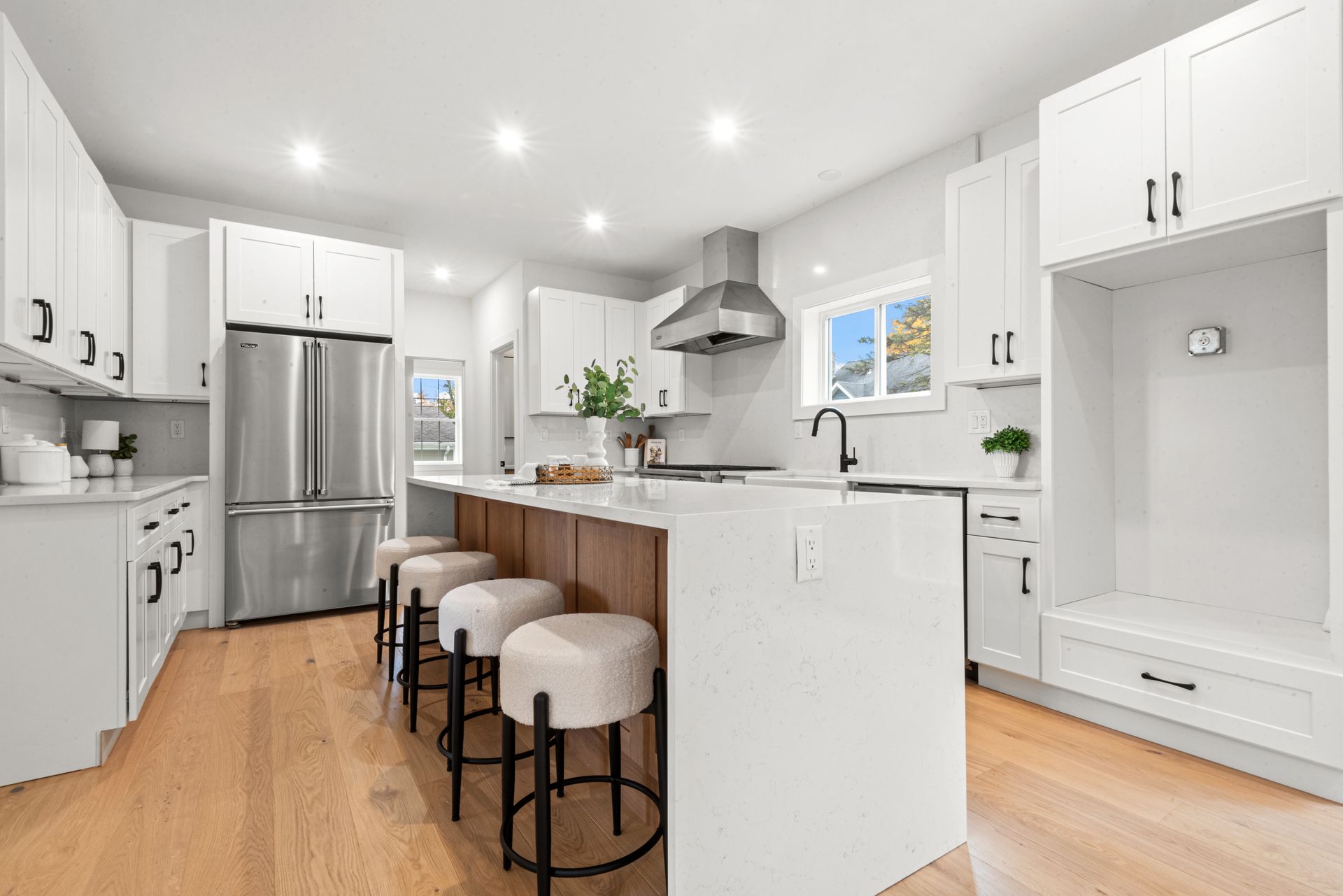 Modern white kitchen with island, stainless steel appliances, and wooden floor.