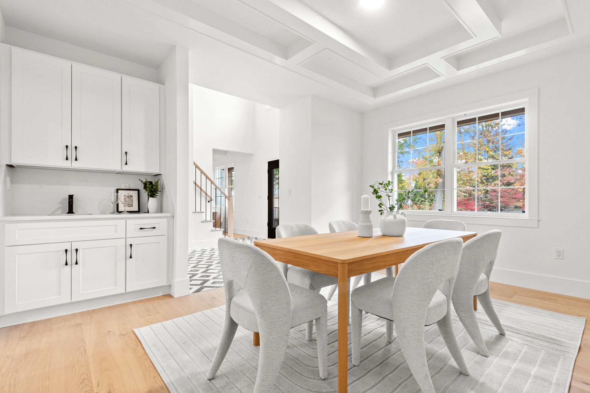 White dining room with a wooden table, six chairs, cabinets, and a window.