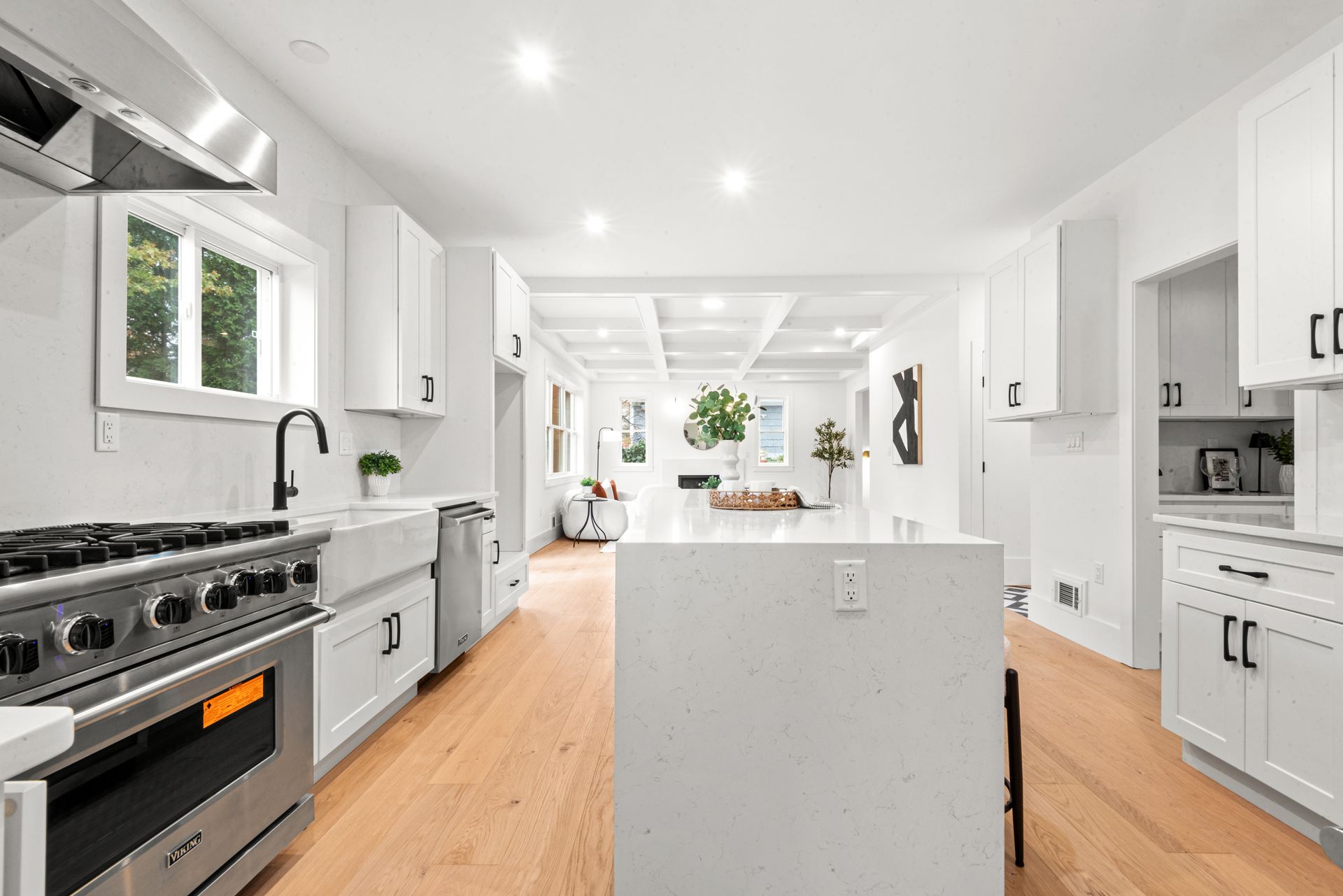 Bright white kitchen with stainless steel appliances, white cabinets, and wooden floors.