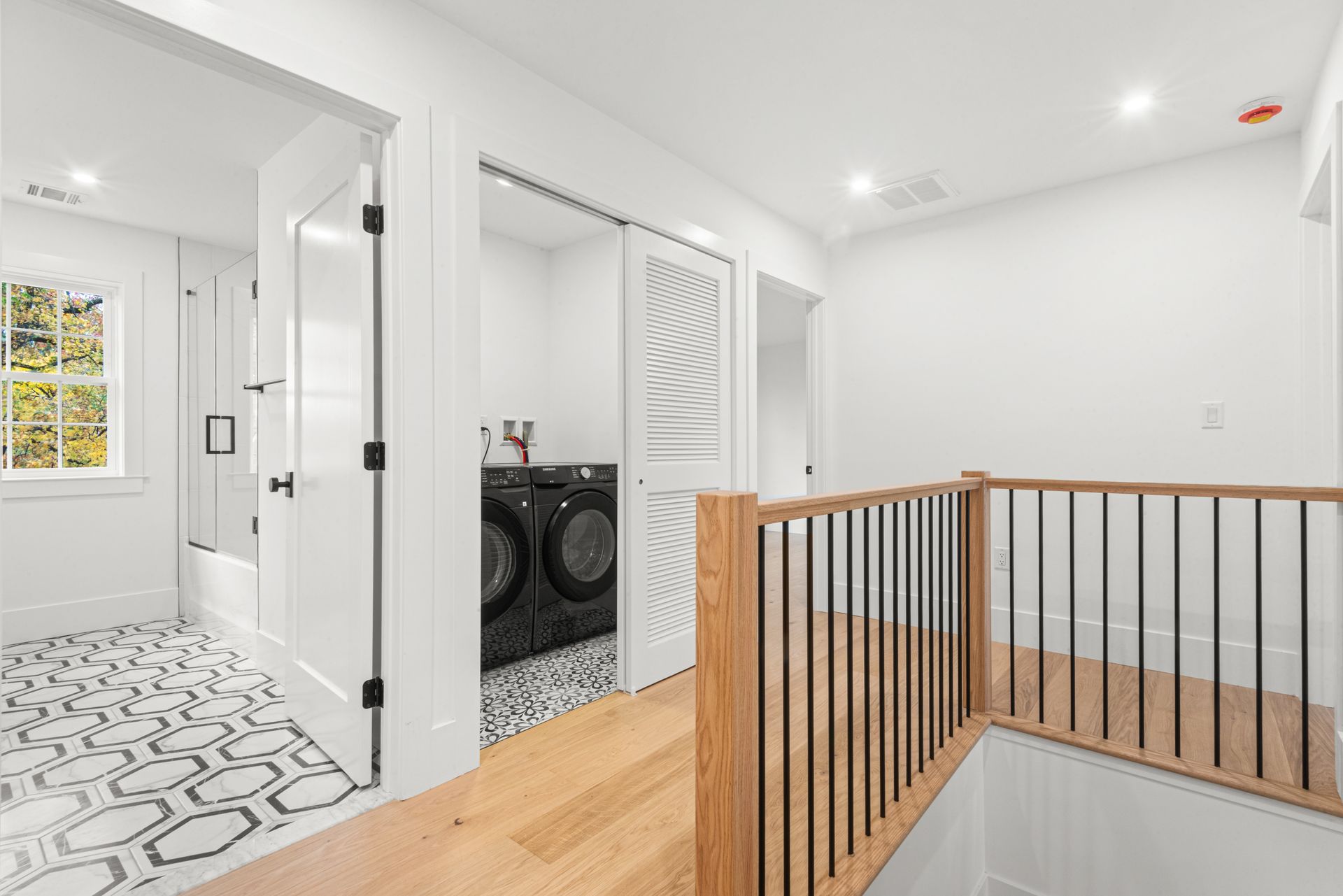 Bright hallway with laundry room, bathroom, and a railing over a lower level.