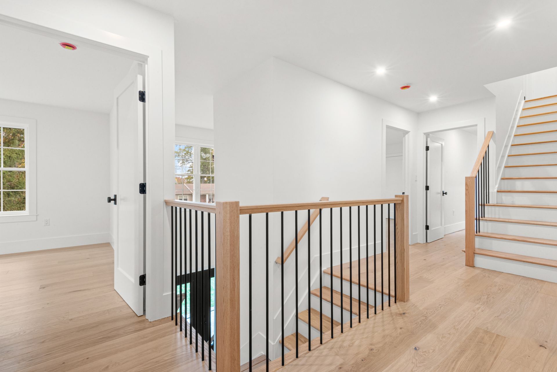 Hallway with light hardwood floors, white walls, black railing, and staircase.