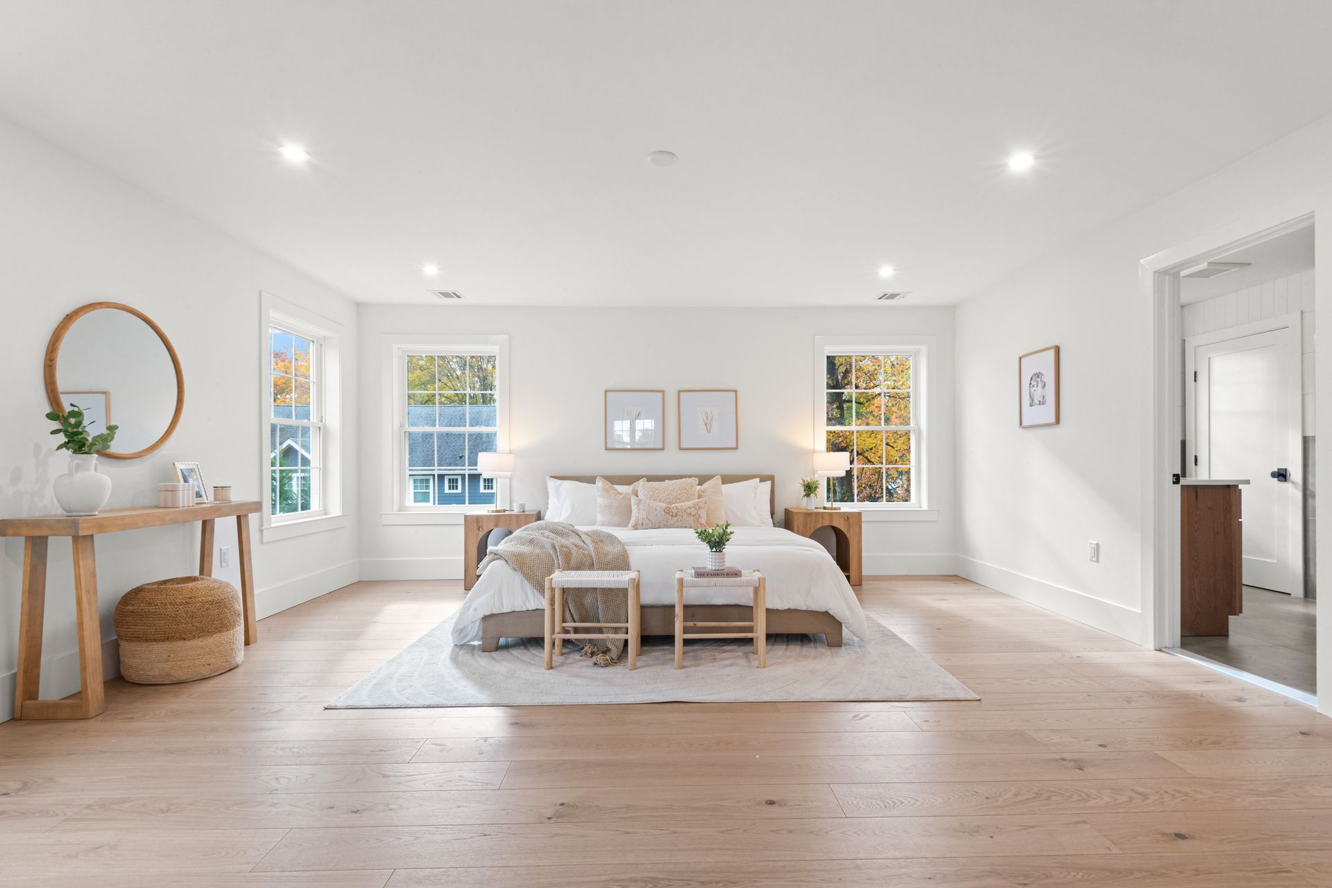 Spacious white bedroom with light wood floors, a large bed, two side tables, and natural light.