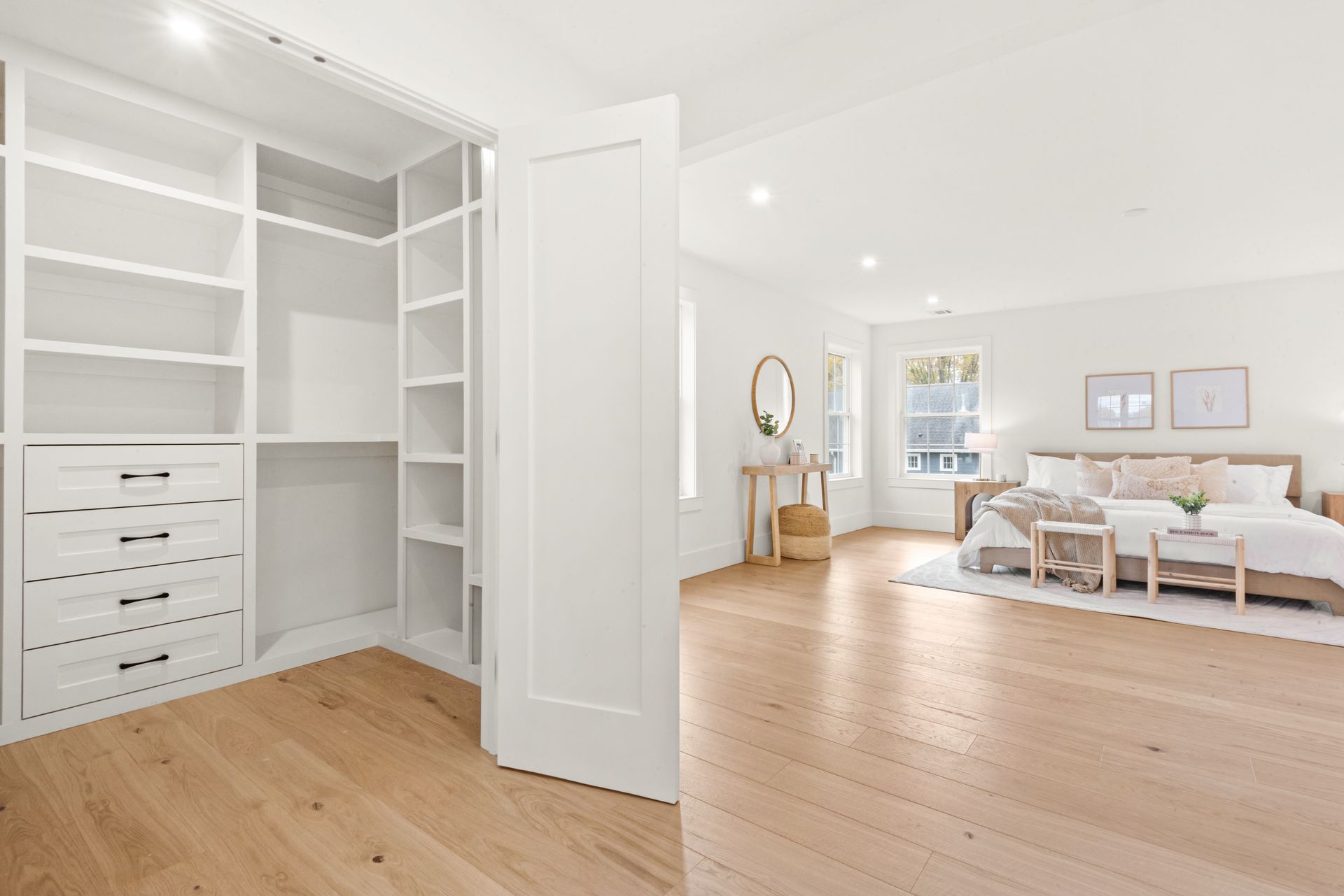 Bright white bedroom with walk-in closet, wooden floors, and a bed in the background.