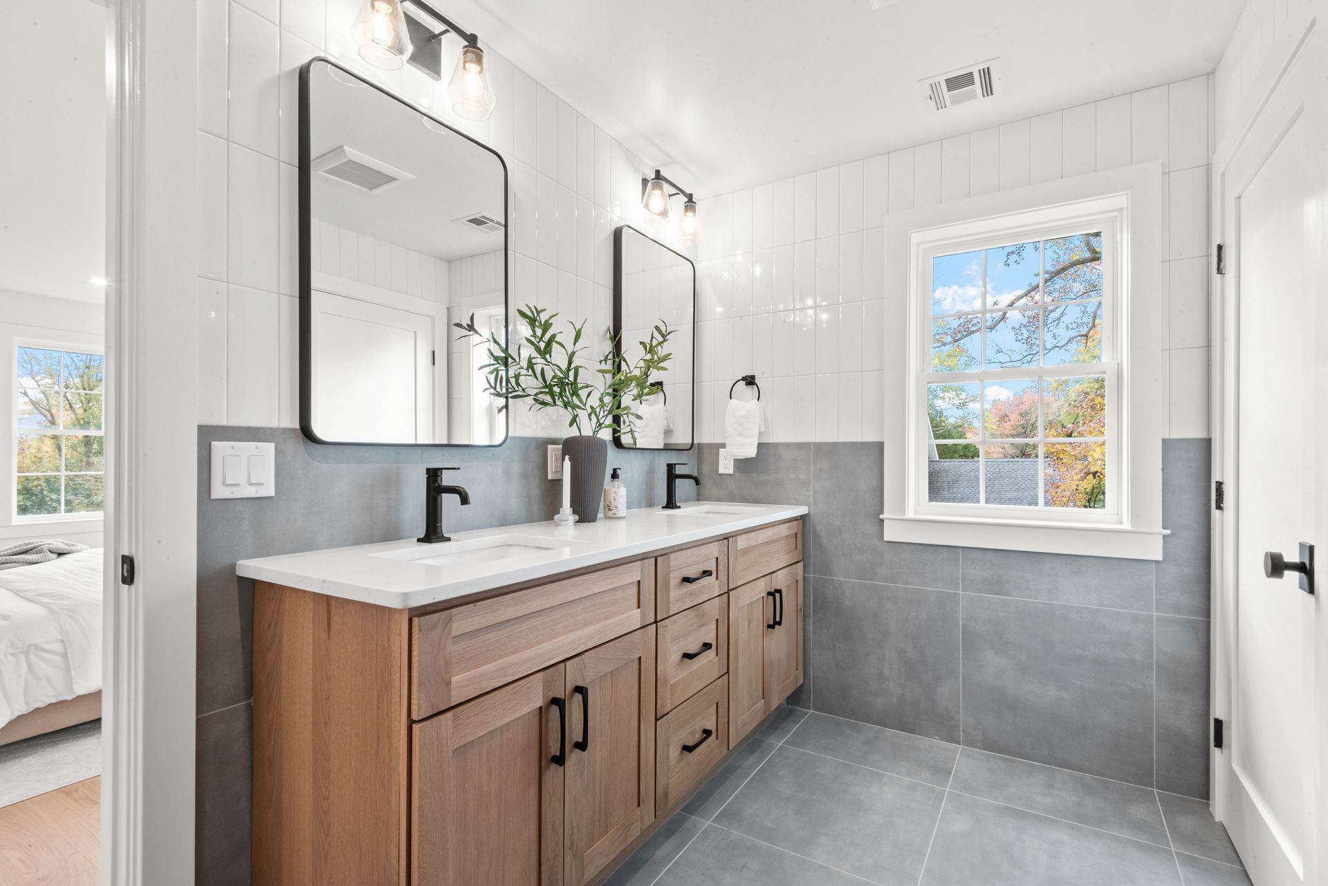 Bathroom with a double vanity, large mirrors, and a window with a view of trees. Gray and white color scheme.