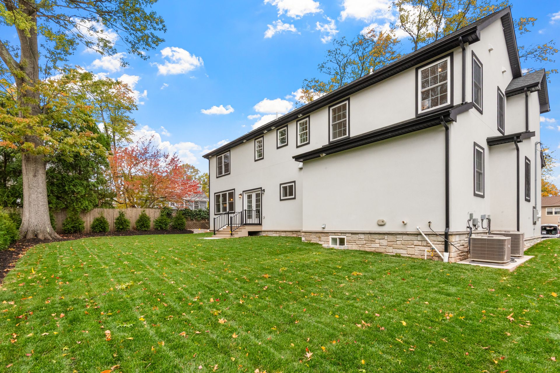 Rear exterior of a white two-story house with green lawn, trees, and blue sky with clouds.