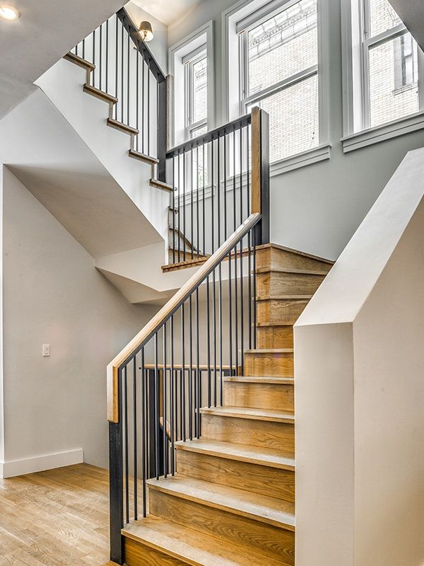 Row of brownstone buildings with windows, stairs, and ornamental iron fences.