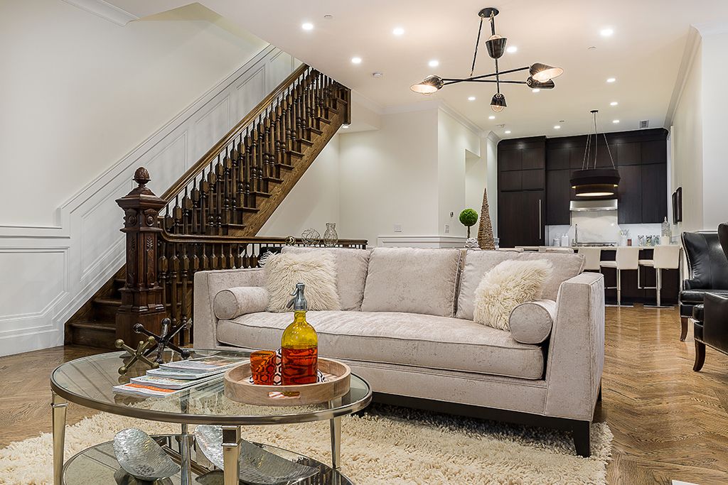 Living room with staircase, sofa, coffee table, and open kitchen with dark cabinets.