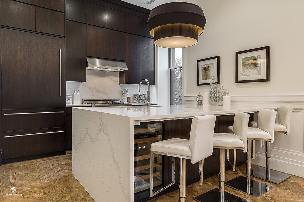 Modern kitchen with dark wood cabinets, white island with seating, and pendant light fixture.